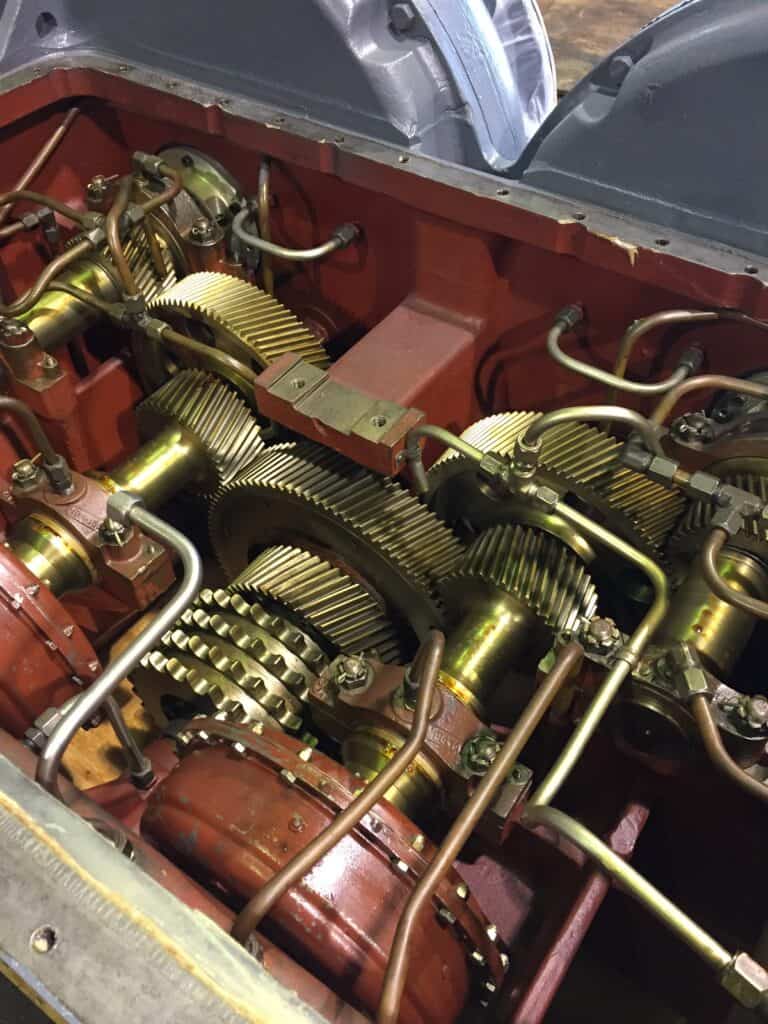 Close-up view of an exposed mechanical gearbox with interlocking brass gears and metal pipes inside a red housing.
