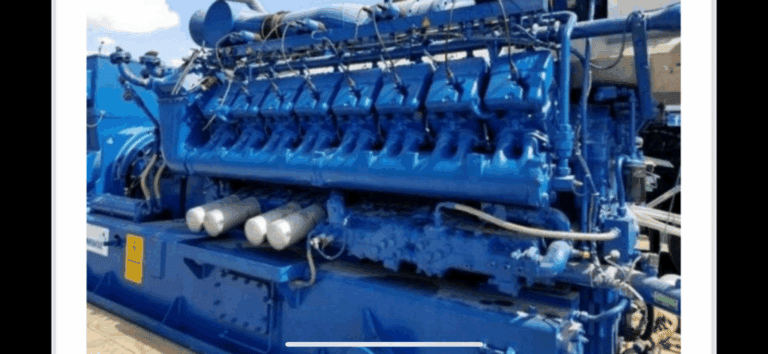 Large industrial blue engine generator with multiple cylinders and pipes, positioned outdoors on a concrete surface.